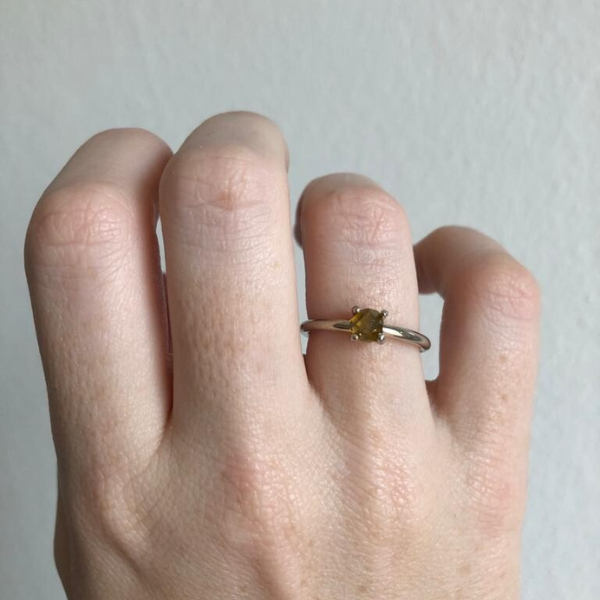 Hand wearing a silver ring with a green gemstone on a plain background