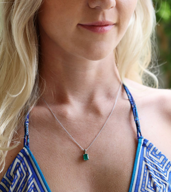 Woman wearing a blue and white patterned top with a necklace featuring a green pendant.
